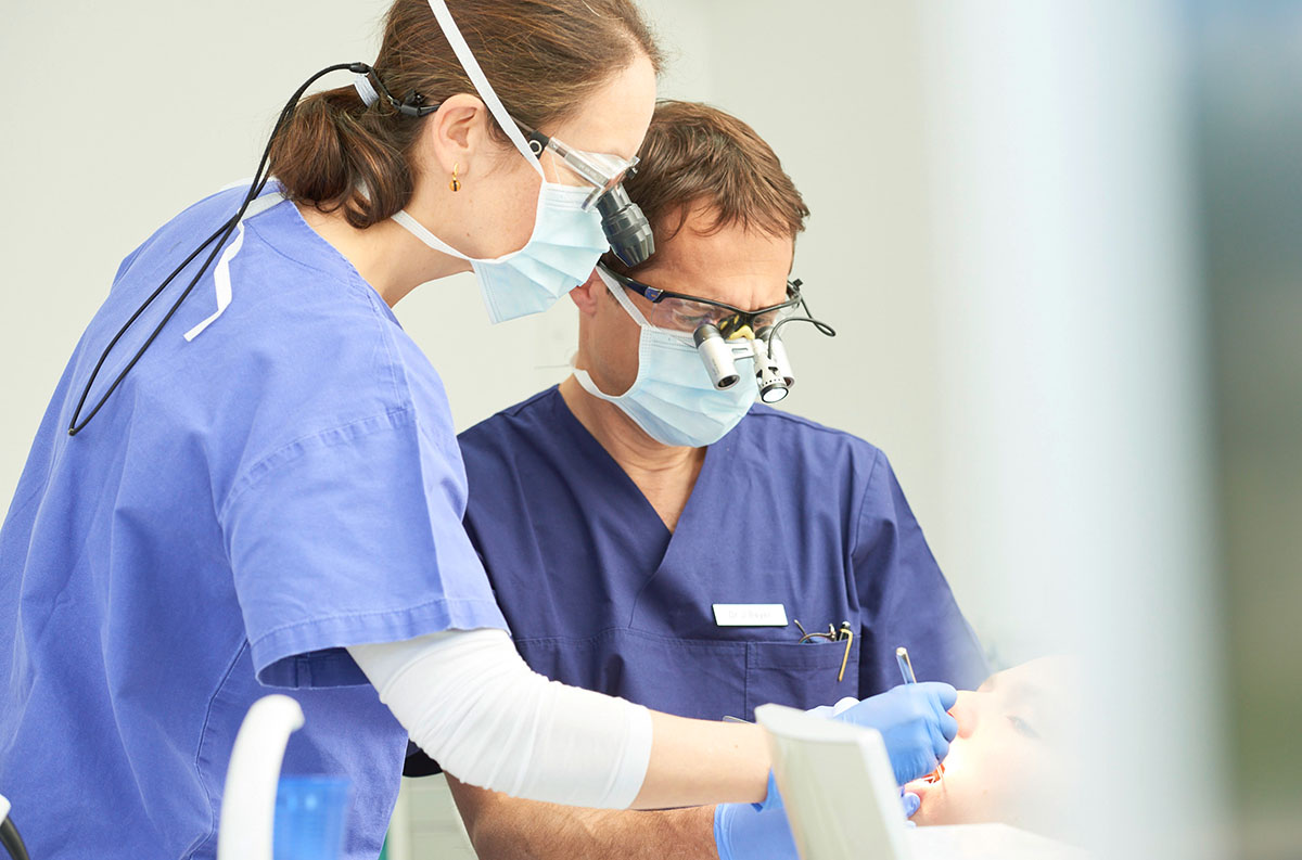 Impressionen: 2 Ärzte untersuchen eine Patientin an, die auf dem Behandlungsstuhl sitzt
